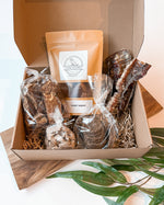 Open Wild Roots Box with natural dog treats including rabbit jerky, venison liver, bison lung, duck cookies, and bison trachea displayed on earthy packaging.