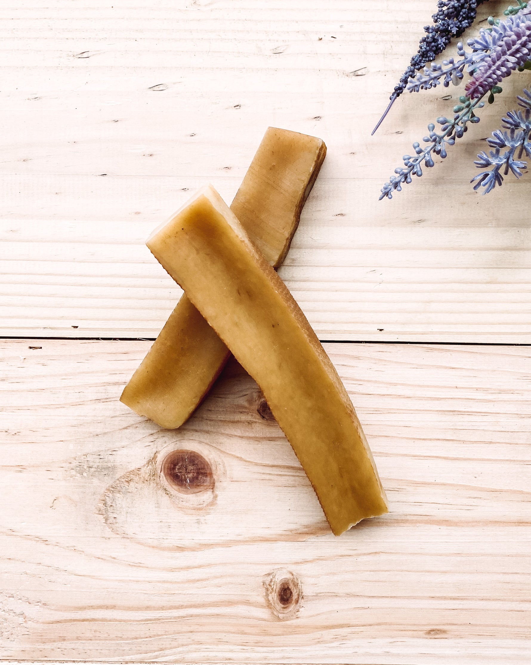 Two yak chews placed on a wooden surface with a sprig of lavender in the top right corner.